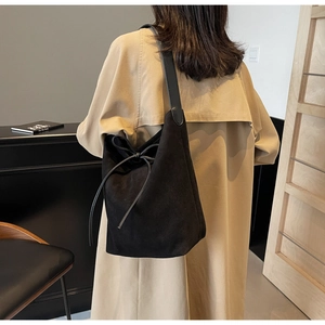 Detail of black suede tote bag with bow drawstring and sleek leather strap on shoulder