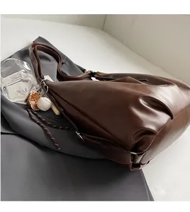 Dettaglio di una borsa tote in pelle marrone con ciondolo da baseball su blazer grigio