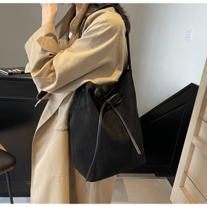 Detail view of a black nylon tote bag with a bow drawstring on a trench coat model