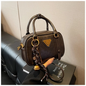 Detailansicht der braunen Mini-Boston-Tasche aus Leder mit goldenem Logo und Anhänger