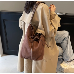 Close-up of brown suede shoulder bag with thin bow detail on autumn trench coat