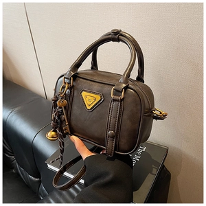 Detailansicht der dunkelbraunen Boston-Tasche mit gelbem Logo und goldenen Anhängern