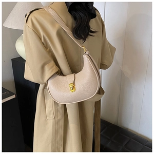 Detail view of beige crescent bag with lychee texture and golden metal clasp on a model