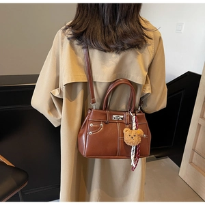Detail of vintage brown leather satchel featuring contrast stitching and plush bear charm