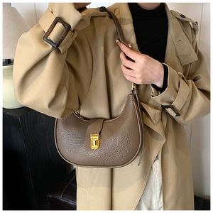 Detail of dark brown lychee leather hobo bag with gold clasp on khaki trench coat