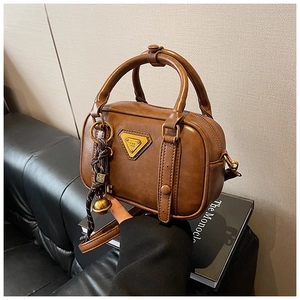Detail der braunen Vintage Umhängetasche mit goldenem Dreieckslogo und Anhänger