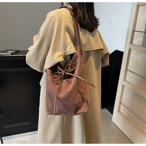Detail of vintage brown suede bucket bag with leather bow decoration on trench coat