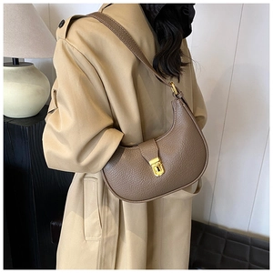 Brown pebbled leather crescent bag with gold buckle worn on model's shoulder