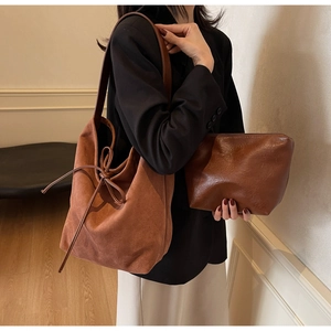 Close-up of brown suede bucket bag featuring a large decorative bow on shoulder strap
