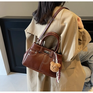 Brown leather handbag detail featuring white stitching and a plush bear charm decoration