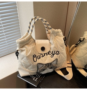 Detail der cremefarbenen Stepptasche mit Plüschkatze und gewebtem Tragegriff