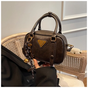 Detail der braunen Vintage-Handtasche mit goldenem Logo und dekorativem Glockenanhänger