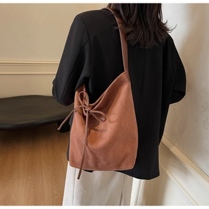 Close-up of caramel suede tote bag featuring a decorative long tassel bow and soft texture