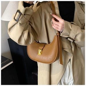 Detail of a brown leather crescent dumpling bag with a gold buckle on a casual outfit