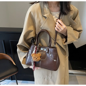 Detail of dark brown leather handbag featuring white stitching and bear charm accessory
