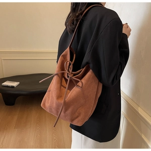 Detail of terracotta suede tote bag with tie-knot bow and shoulder strap on black blazer