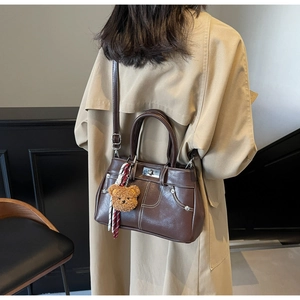 Detail of dark brown vintage oil leather bag with contrast stitching and teddy bear charm