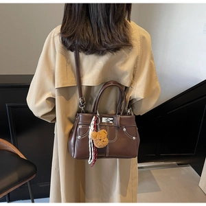 Detail of dark brown faux leather handbag featuring white stitching and bear charm on model