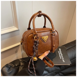 Close-up of vintage brown leather handbag featuring metal triangle logo and woven tassel