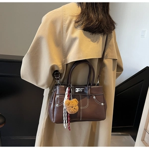 Dark brown leather handbag with contrast stitching and plush bear charm shown on model