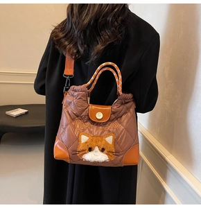 Detail einer braunen Stepp-Tote-Bag mit Katzenstickerei und orangem Schultergurt