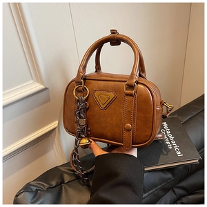 Close-up of vintage brown leather bowling bag with gold bell charm and triangular logo