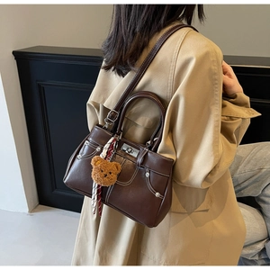 Close-up of vintage brown leather handbag with contrast stitching and teddy bear charm