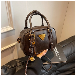 Detailed view of dark brown faux leather boston bag with gold triangle logo and tassel charm