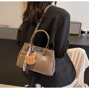 Detail of brown trapezoidal satchel with white contrast stitching and silver twist-lock