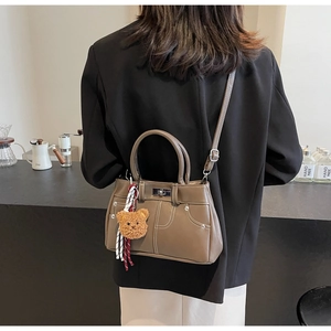 Detail of khaki leather handbag with contrast stitching and plush bear charm accent