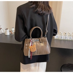 Brown vintage handbag with white stitching and cute teddy bear charm on a coffee shop table