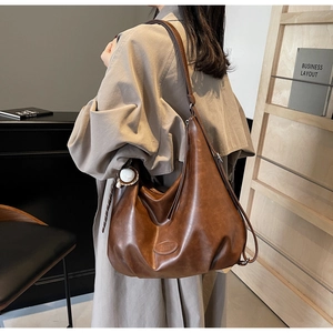 Dettaglio laterale della grande borsa tote marrone in ecopelle con pendente da baseball