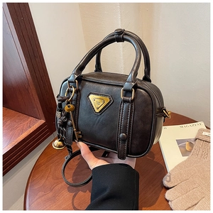 Detail of vintage brown leather handbag featuring metal logo and decorative charm