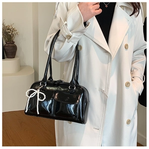 Détail du sac Boston en cuir verni noir avec un accessoire de nœud en perles tressées