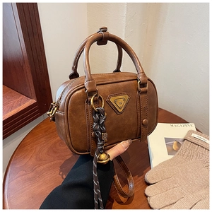 Detail of vintage brown leather handbag with metallic logo and braided rope charm on wood