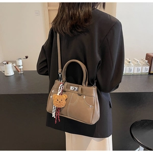 Detail of khaki leather crossbody bag with white stitching and plush bear charm accessory