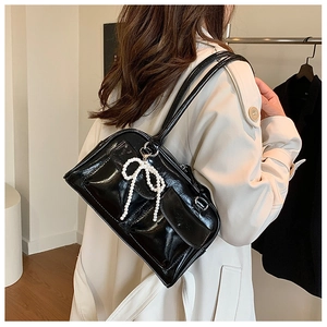 Vue latérale d'un sac Boston noir verni avec nœud en perles sur un manteau beige