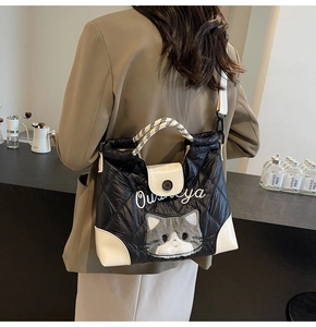 Detail einer schwarzen Stepptasche mit Katzenstickerei und weißem Webgurt