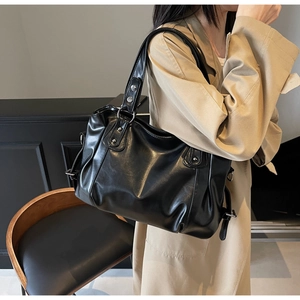 Vue latérale d'un grand sac cabas noir en cuir souple avec détails de boucles en métal