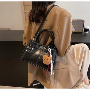 Detail of vintage black crossbody bag with white stitching and plush bear charm