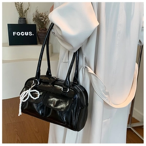 Détail du sac Boston en cuir verni noir avec breloque nœud en perles et poches avant