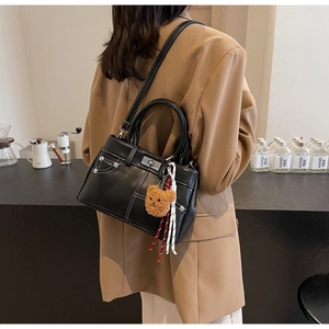 Detail of vintage black leather handbag with white stitching and bear charm