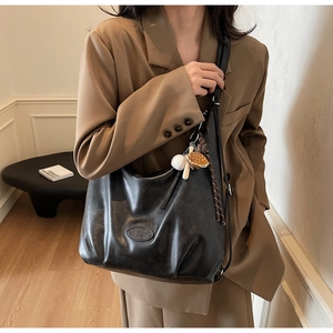Dettaglio borsa hobo nera con ciondolo da baseball su modella in studio minimalista