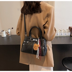 Detail of vintage black leather handbag with white stitching and cute bear charm