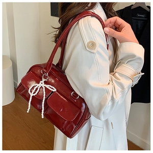 Détail du sac Boston en cuir verni bordeaux avec double poche et pendentif nœud en perles