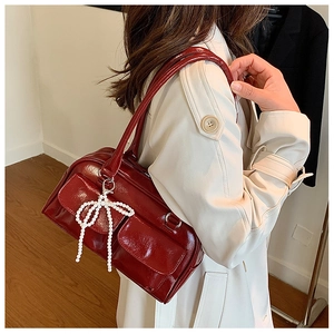 Détail du sac Boston en cuir verni bordeaux avec rabats de poche et nœud en perles