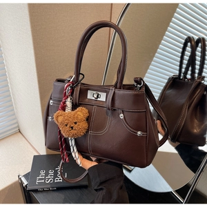 Close-up of vintage coffee brown PU leather handbag with white stitching and bear charm