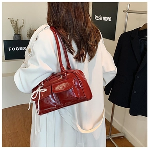 Détail du sac Boston en cuir verni rouge avec fini brillant et breloque nœud en perles