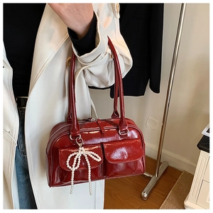 Détail du sac Boston en cuir verni rouge avec nœud en perles et fini brillant