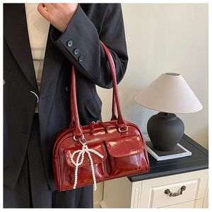 Détail du sac Boston en cuir verni bordeaux avec charm nœud en perles et deux poignées